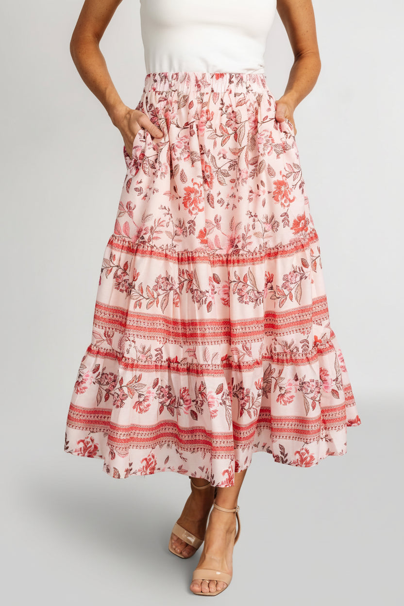 Model front view wearing Meg tiered midi skirt in blush multi floral print, showing smocked elastic waistband, soft tiers, and side pocket detail.