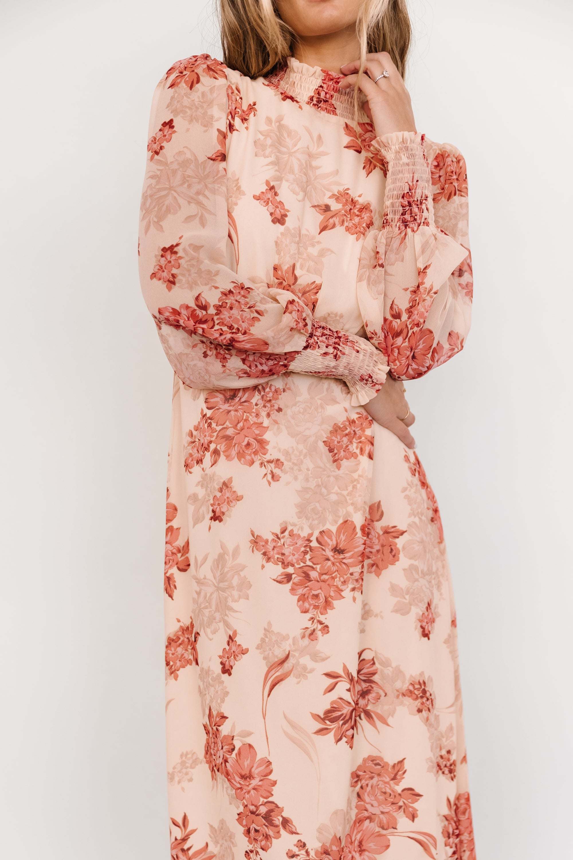 Model wearing Luciana maxi dress walking to show skirt movement and tiered silhouette in beige and rose floral chiffon material.