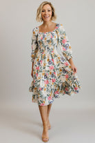 Front view of a smocked midi dress in muted multi floral print on a model, showing square neckline and tiered skirt, full-length.
