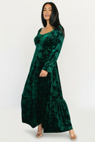 Styled look of the Audra emerald velvet dress in a holiday setting, showing overall fit, movement and embossed floral detail.