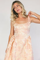 Model wearing a peach floral jacquard midi dress with a square neckline, wide tank straps, and a fitted bodice.