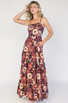 Model wearing a deep berry floral maxi dress with a square neckline, adjustable spaghetti straps, and a smocked back bodice.