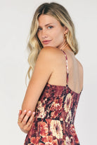Model wearing a deep berry floral maxi dress with a square neckline, adjustable spaghetti straps, and a smocked back bodice.