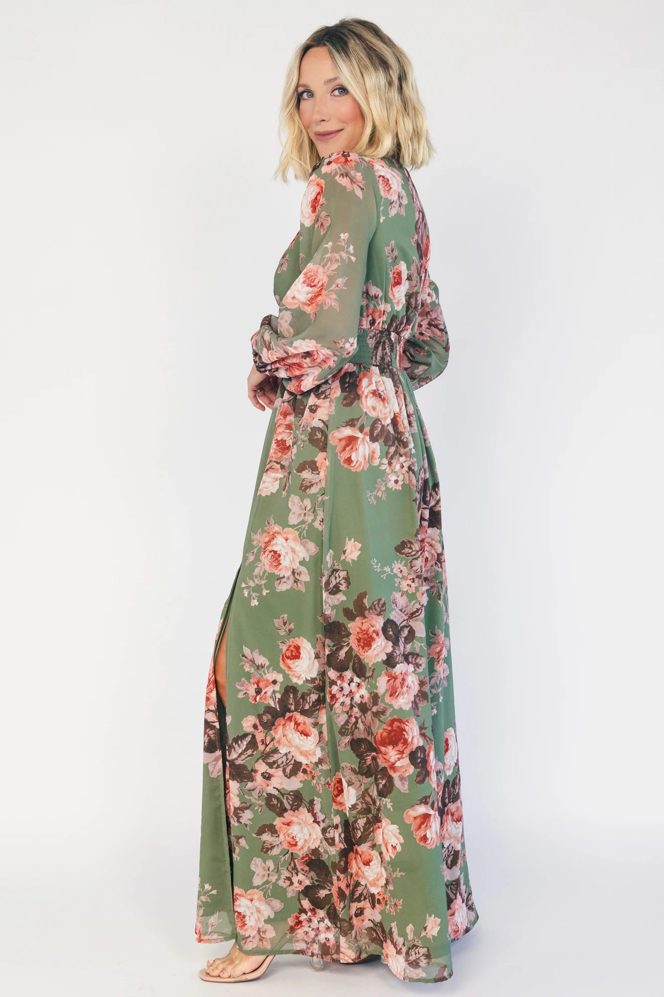 Model wearing a green floral maxi dress with a V-neckline, long bishop sleeves, and a gathered waist with a smocked back.