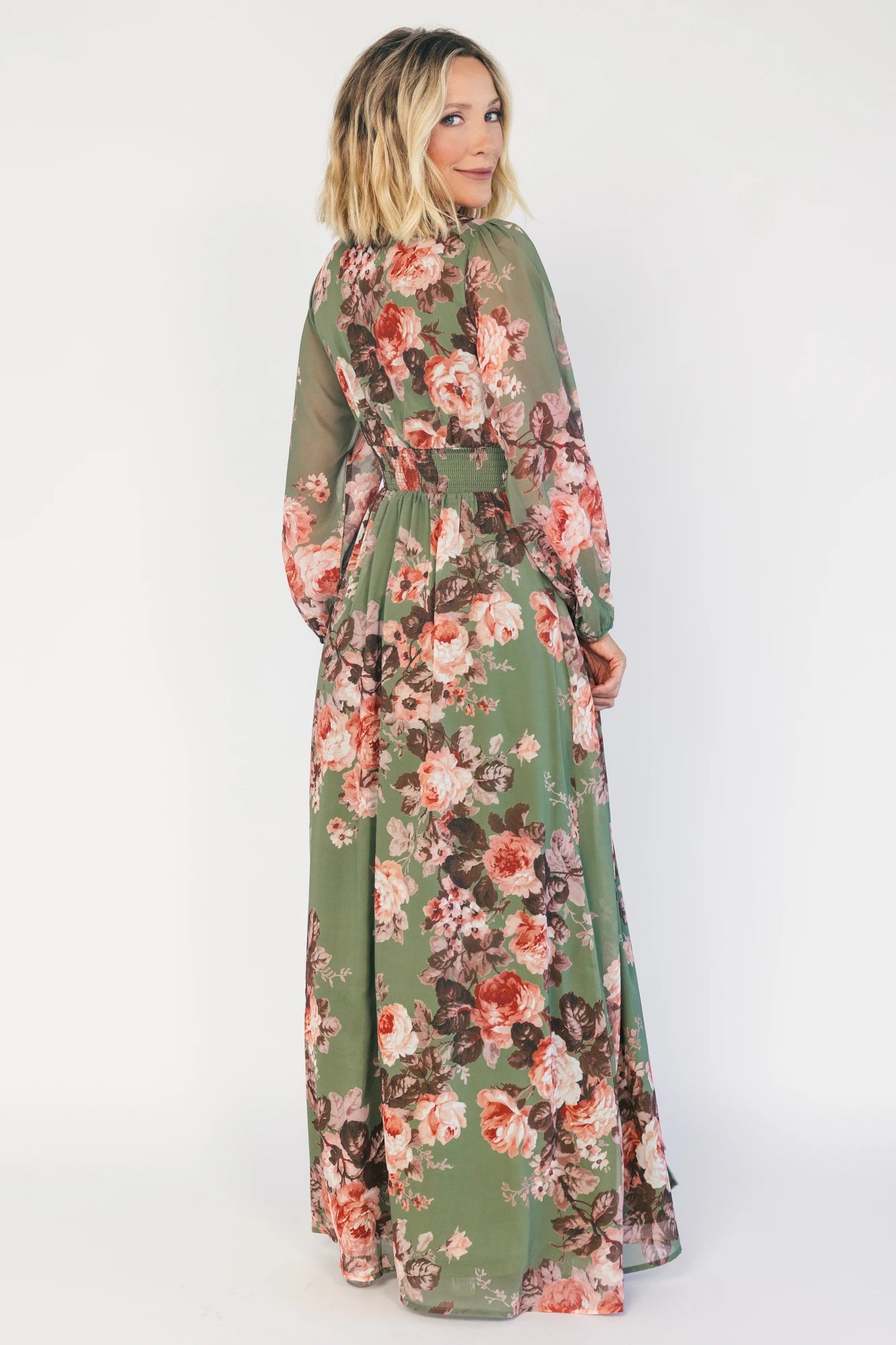 Model wearing a green floral maxi dress with a V-neckline, long bishop sleeves, and a gathered waist with a smocked back.