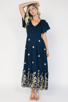 Model wearing a navy embroidered maxi dress with a V-neckline, flutter sleeves, and a smocked bodice.