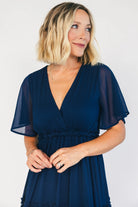 Model wearing a navy chiffon maxi dress with a surplice V-neckline, short ruffled sleeves, and an elastic empire waist.