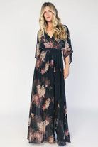 Model wearing a black floral maxi dress with a surplice V-neckline, kimono sleeves, and an elastic waist with a removable sash tie.