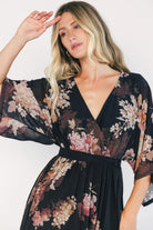 Model wearing a black floral maxi dress with a surplice V-neckline, kimono sleeves, and an elastic waist with a removable sash tie.