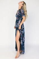 Model wearing a deep blue floral maxi dress with a deep V-neckline, short flutter sleeves, and an empire waist.