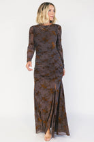 Model wearing a clove maxi dress with copper velvet burnout detailing, a high round neckline, and long sheer sleeves.