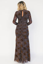 Model wearing a clove maxi dress with copper velvet burnout detailing, a high round neckline, and long sheer sleeves.