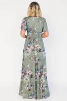 Model wearing a sage floral maxi dress with a deep V-neckline, short flutter sleeves, and an empire waist.