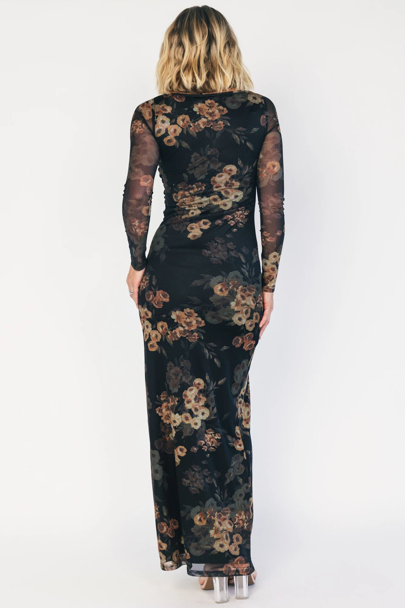 Black mesh bodycon midi dress with muted gold floral print, sheer long sleeves, a round neckline, flattering side ruching, and a thigh-high side slit.