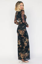 Black mesh bodycon midi dress with muted gold floral print, sheer long sleeves, a round neckline, flattering side ruching, and a thigh-high side slit.