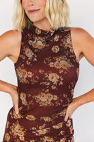 Model wearing a mahogany floral maxi dress with a high neckline, sleeveless fitted bodice, and ruched side detailing.