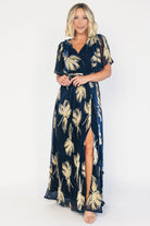 Navy and gold shimmer maxi dress with a surplice V-neckline, sheer sleeves, an elastic waist with a removable sash tie, and a flowing full-length skirt with a side slit.