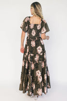 Dark olive floral maxi dress with a smocked bodice, square neckline, flutter sleeves, and a tiered ruffle skirt.