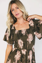 Dark olive floral maxi dress with a smocked bodice, square neckline, flutter sleeves, and a tiered ruffle skirt.