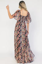 Model wearing a gray floral maxi dress with a sweetheart neckline, flutter sleeves, and a smocked back bodice.