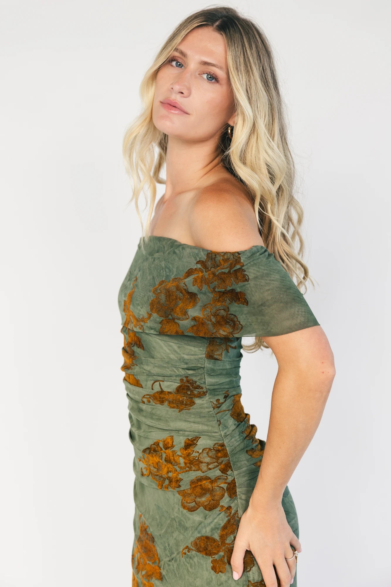 Model wearing an off-the-shoulder maxi dress with a green mesh overlay and copper velvet floral detailing.