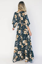 Model wearing a dark jade floral maxi dress with a surplice V-neckline, kimono sleeves, and an elastic waist with a removable sash tie.