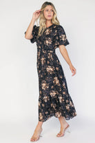 Model wearing a black floral midi dress with a round neckline, puff sleeves, and a smocked waist.