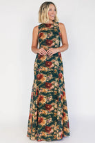Model wearing a topaz floral maxi dress with a high round neckline, sleeveless bodice, and an open back with a sash tie.