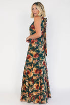 Model wearing a topaz floral maxi dress with a high round neckline, sleeveless bodice, and an open back with a sash tie.