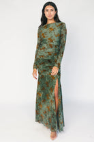 Model wearing a green mesh maxi dress with copper velvet burnout detailing, a high round neckline, and long sheer sleeves.