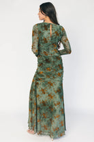 Model wearing a green mesh maxi dress with copper velvet burnout detailing, a high round neckline, and long sheer sleeves.