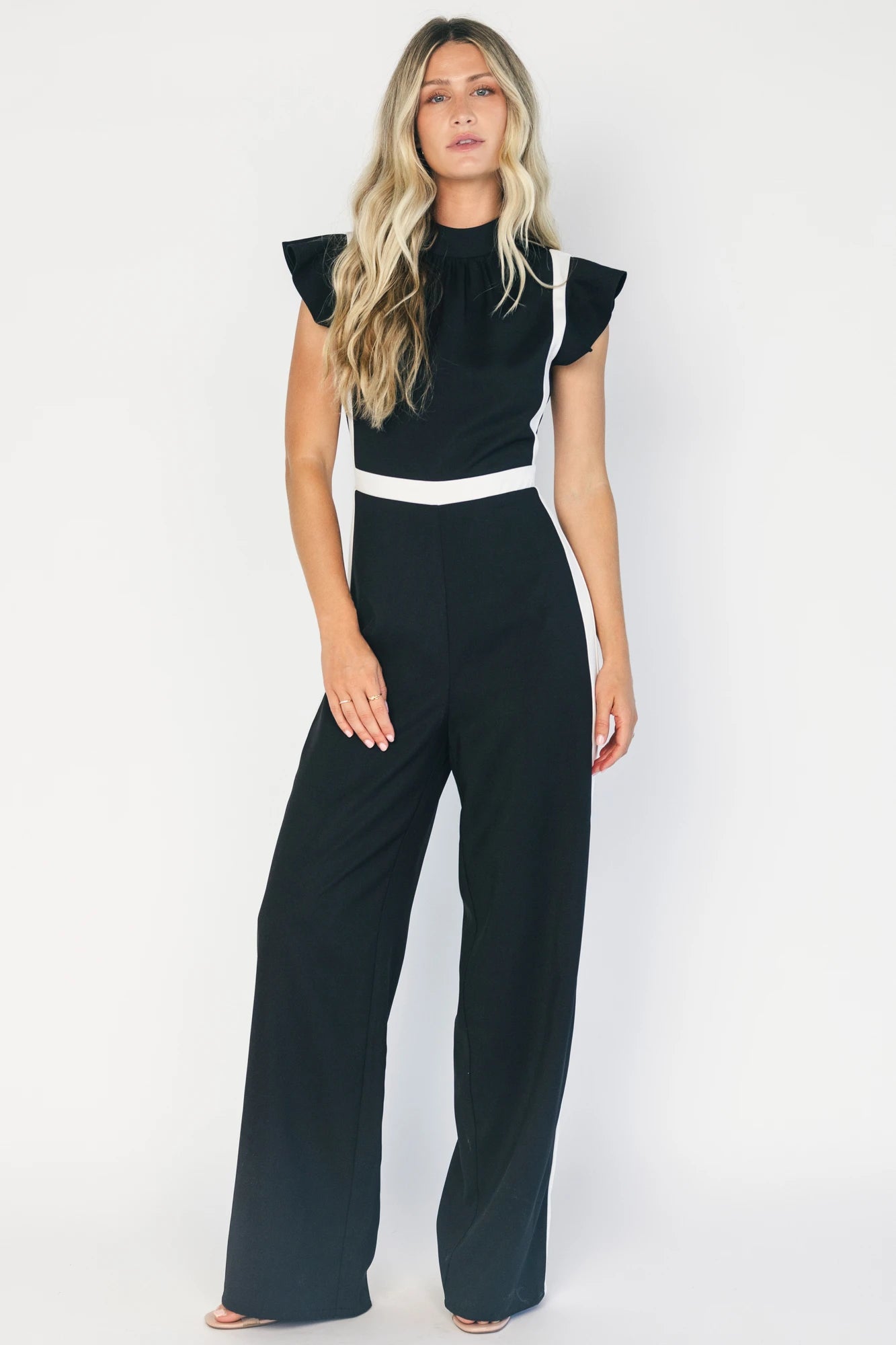 Model wearing the Lumina Ruffle Jumpsuit in Black + Ivory featuring a sleeveless ruffle-trim bodice, defined waist, and flowing wide-leg pants.