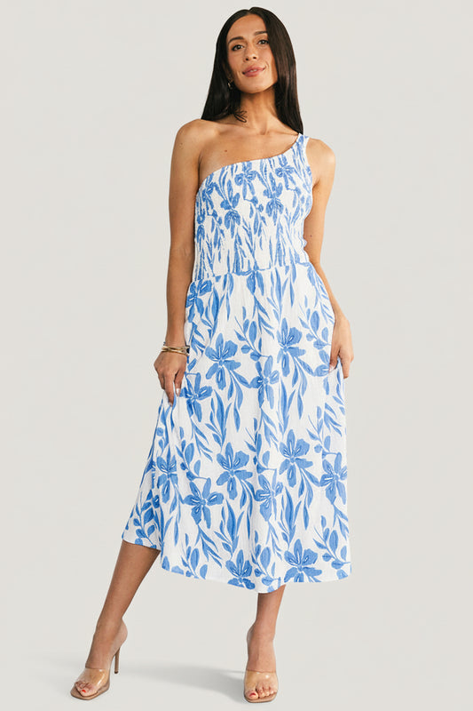 Front full-length view of model wearing Brisa one-shoulder midi dress in white and blue floral print, showing smocked bodice and asymmetric neckline.