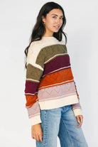 Ivory striped sweater with green, mulberry, rust, and purple horizontal stripes, a round neckline, dropped shoulders, long sleeves, and a relaxed fit.