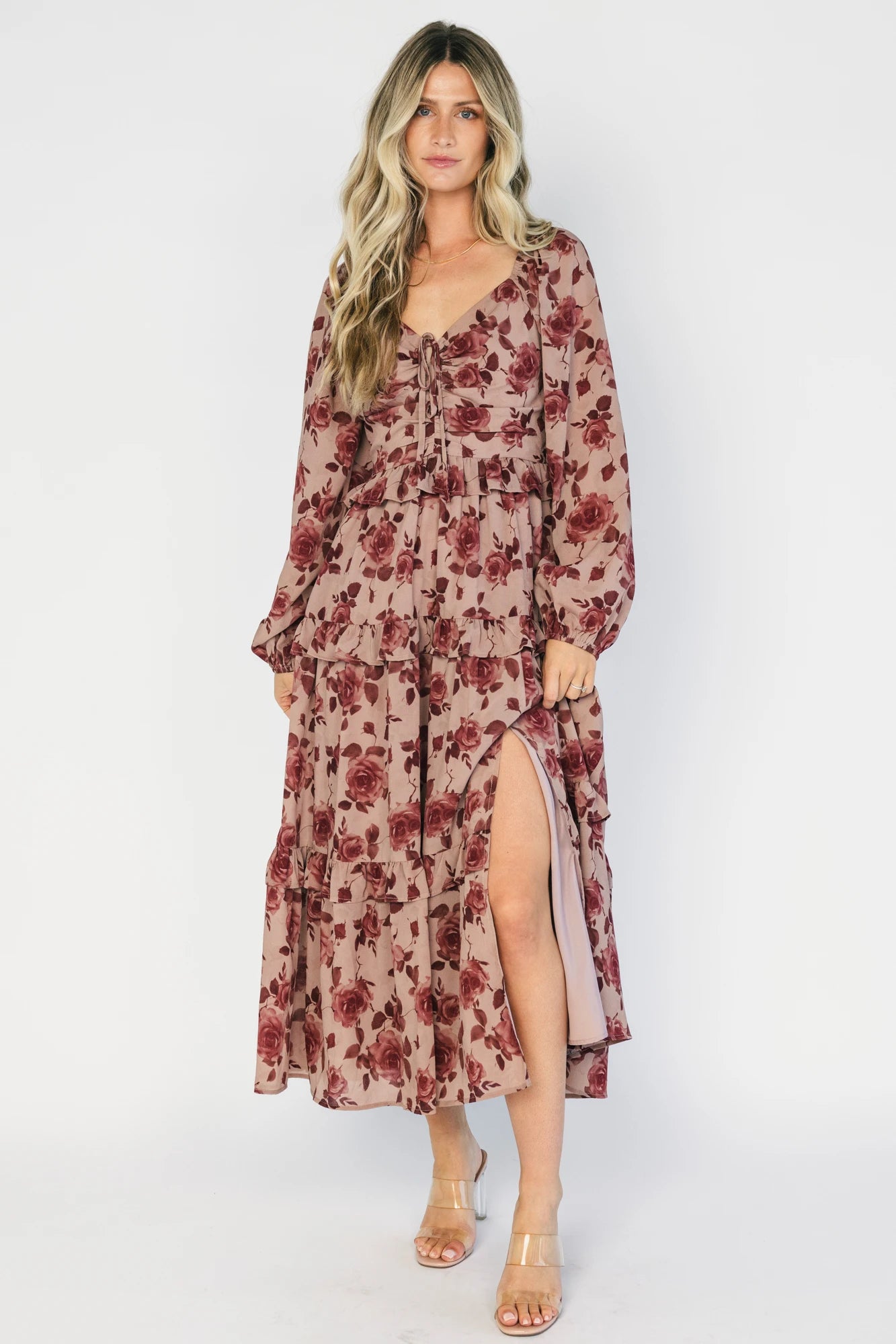 Model wearing a dusty mauve floral maxi dress with a sweetheart neckline, adjustable tie-front bust, and long sheer sleeves.