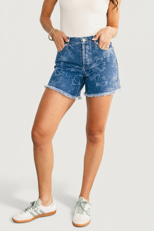 Front view of medium-wash high-rise jean shorts with laser-printed floral pattern, button-front closure, frayed hem, and functional pockets, on model.