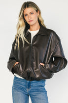Model wearing a dark brown faux leather bomber jacket with a folded lapel collar, front zipper closure, elastic hem, silver snap cuffs, and front pockets.