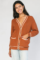 Model wearing a spice orange chunky knit cardigan with a V-neckline, five-button front closure, long sleeves, ribbed trim, front patch pockets, and a relaxed oversized fit.