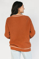 Model wearing a spice orange chunky knit cardigan with a V-neckline, five-button front closure, long sleeves, ribbed trim, front patch pockets, and a relaxed oversized fit.