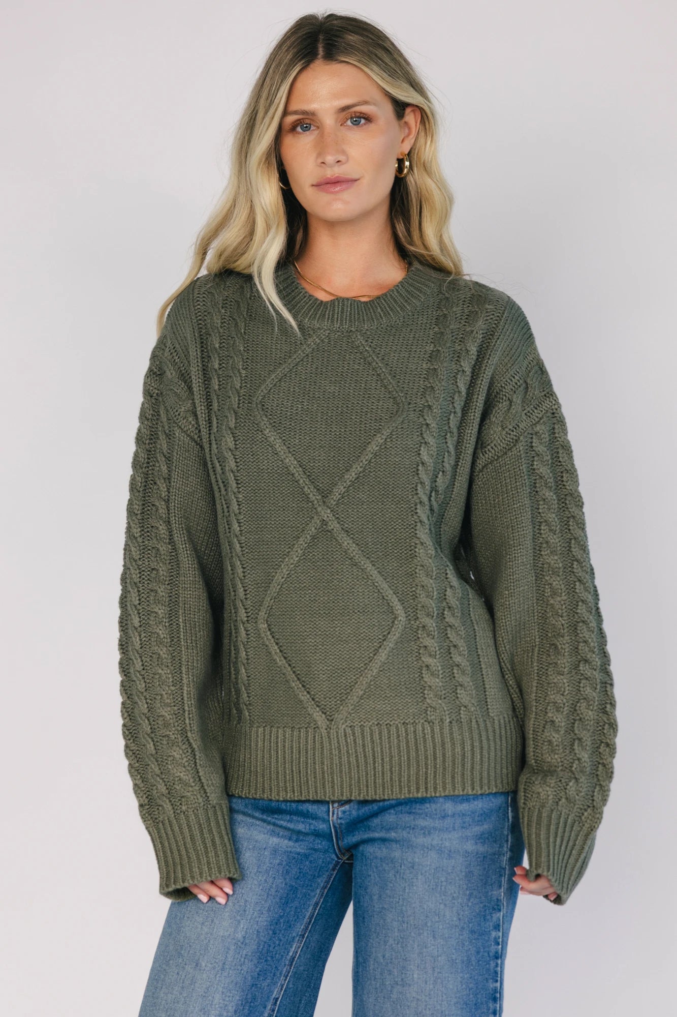 Model wearing an olive knit sweater with a round neckline, long drop-shoulder sleeves, and ribbed trim at the neckline, cuffs, and hem.