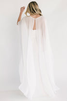 Three-quarter view of gown highlighting pleated skirt movement and soft chiffon cape drape over the arms.
