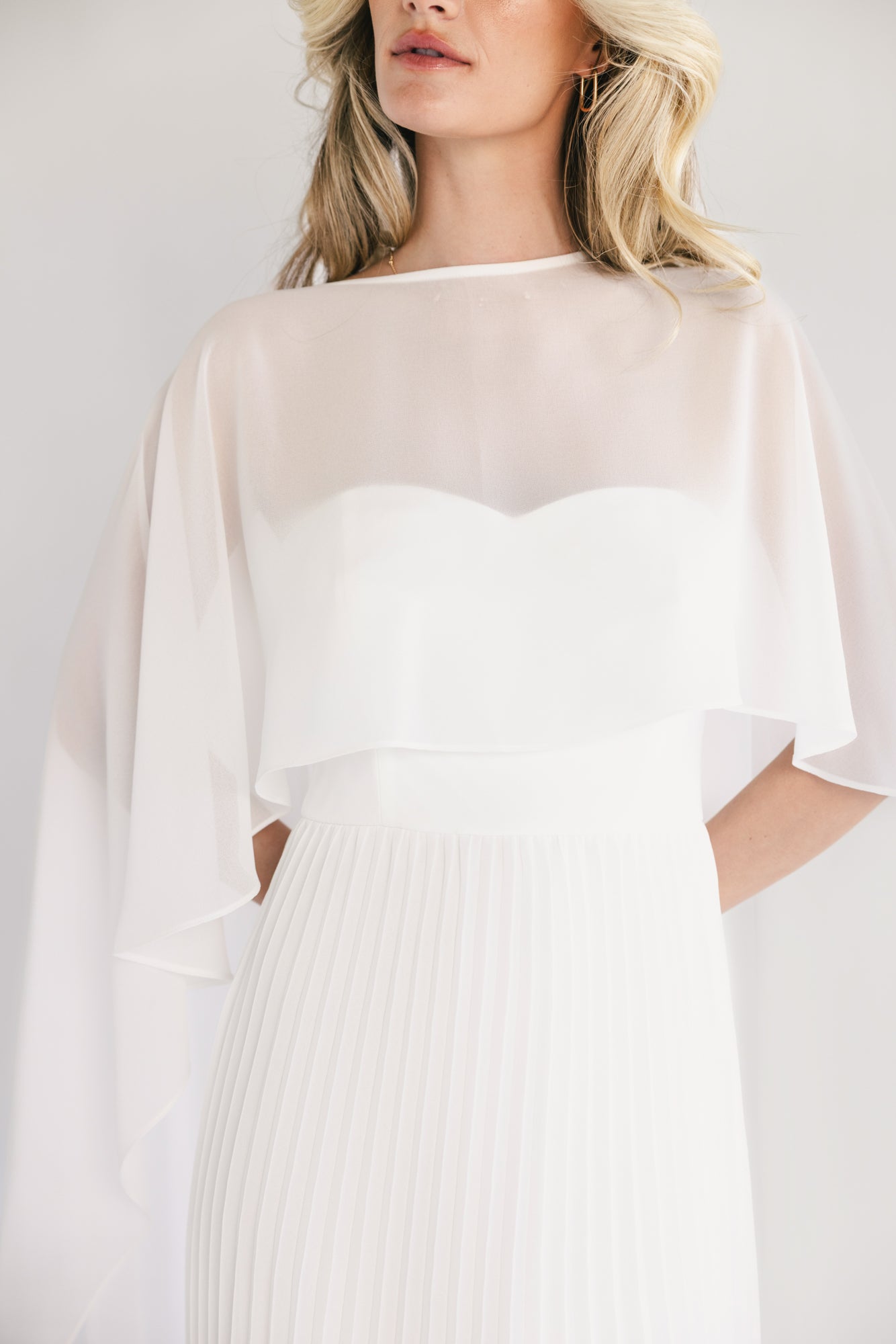 Back view showing button closure at back neck, zip closure, and removable chiffon cape draping over shoulders.