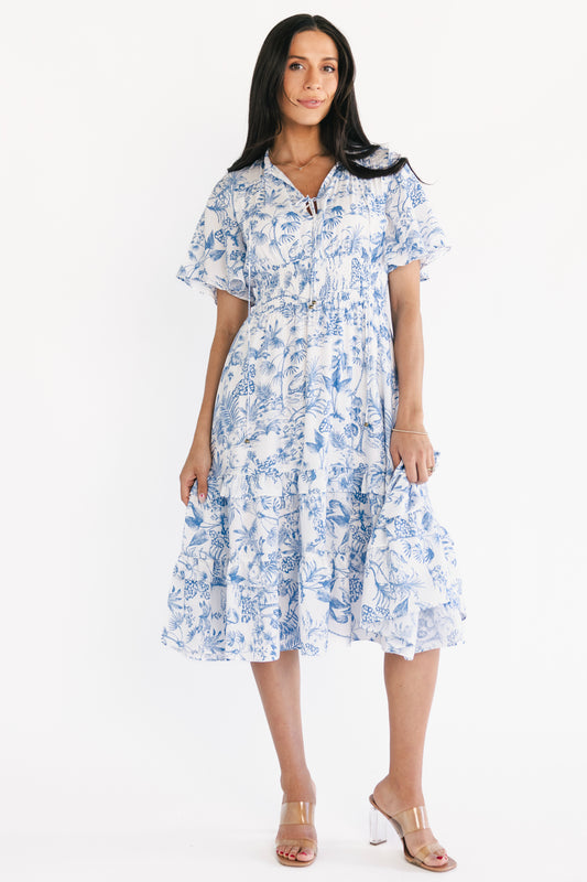 Front view of Willow Boho Midi Dress in white and blue tropical print on a model, showing V-neck, smocked waist, and tiered ruffle skirt, styled for spring events.