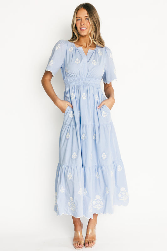 Model wearing the Delilah Embroidered Maxi Dress in light blue, front view showing split V-neck, scalloped short sleeves, embroidered off-white floral pattern and smocked waist.