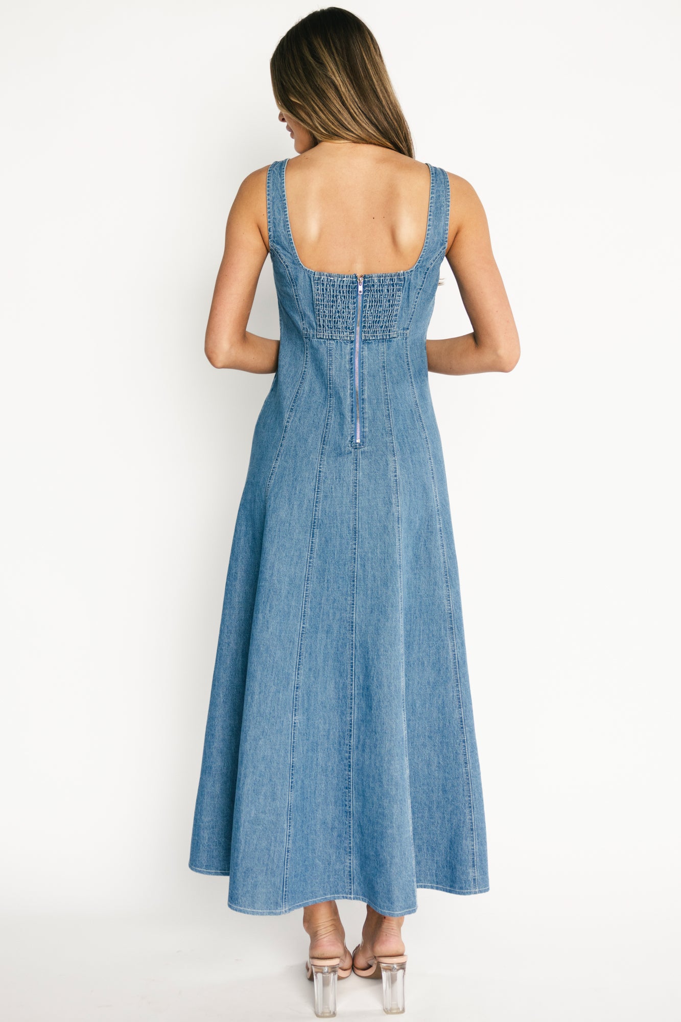 Back view of denim maxi dress highlighting smocked back panel with discreet zipper and unlined 100% cotton construction.