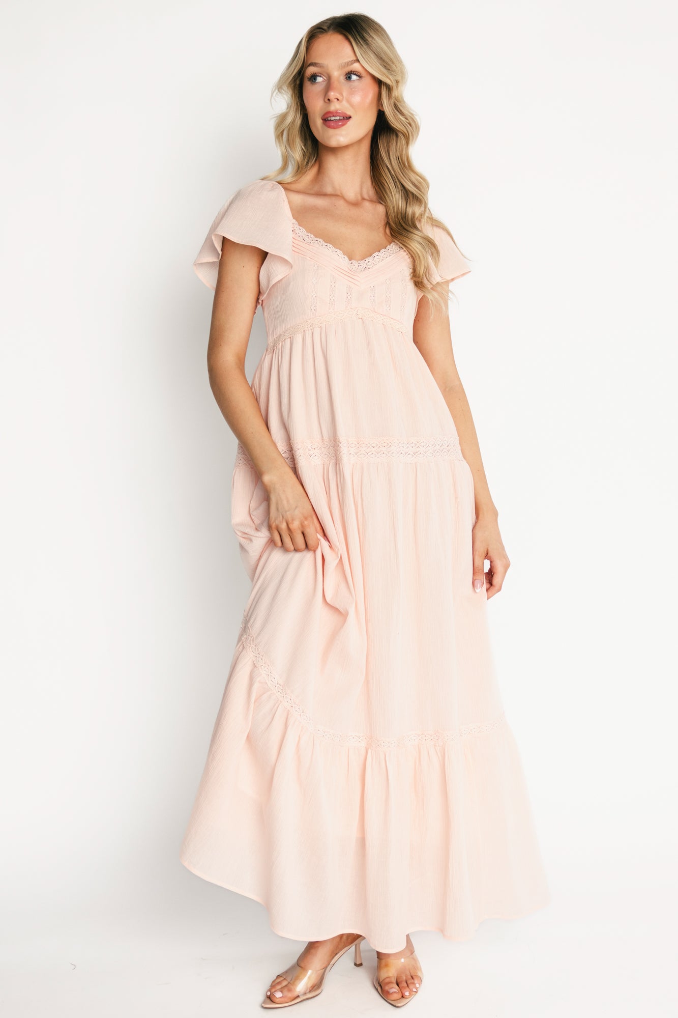 Front view of Sabine Maxi Dress in blush on model, showing V-neck with lace trim, pintuck bodice, flutter sleeves, and tiered maxi skirt in textured cotton.