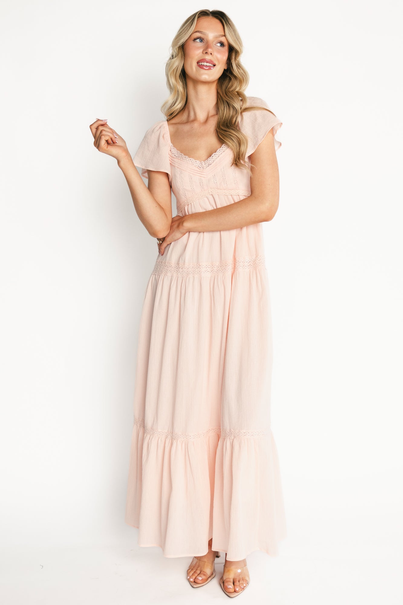 Lifestyle image of Sabine Maxi Dress in blush styled with sandals, showing tiered skirt movement, empire waist, and feminine lace accents on textured cotton fabric.