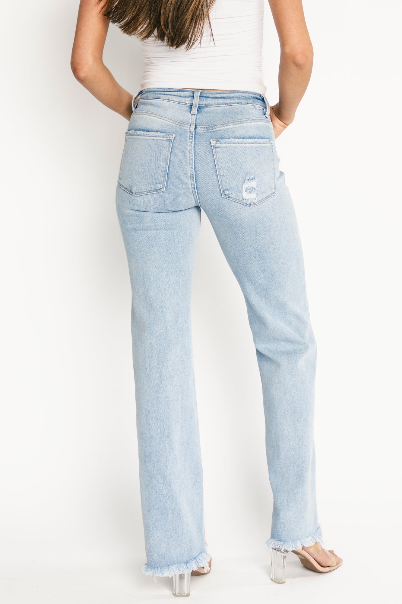 Close-up of denim fabric and distressing on the right back pocket, showing texture, stitch details, and finished frayed edge.