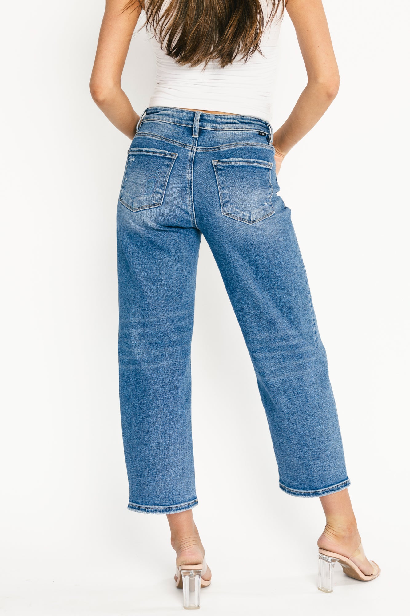 Close-up of Lumi denim fabric and hardware: medium wash, visible weave, light distressing, and button-and-zip fly with clean topstitching details.