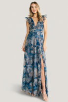 Full-length front view of model wearing Adelyn Maxi Dress in blue floral tulle with deep V-neckline, flutter tank sleeves, banded waist, and left leg slit.